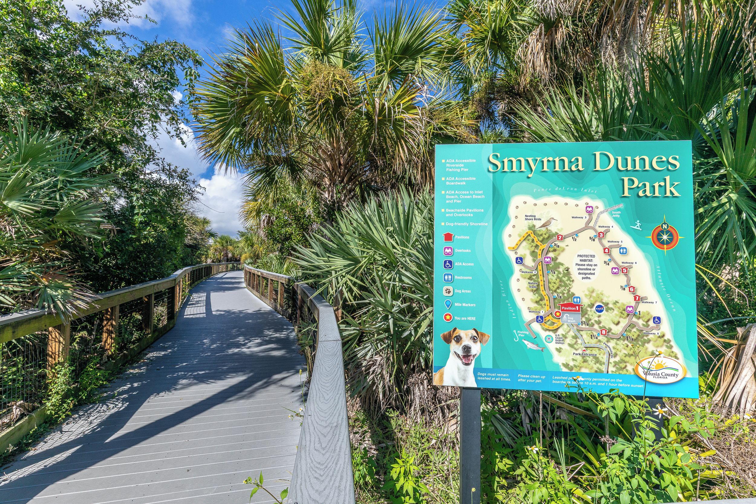 A wooden boardwalk leading through a park with a map and informational sign.