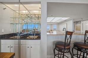A modern kitchen with a glass backsplash, stainless steel appliances, and a bar area with stools. - 🌴Best Views in NSB | XL Oceanfront + Intracoastal Balcony | Minorca Inlet 606🐬 (New Smyrna Beach)