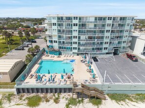 A multi-story hotel with a rooftop pool area, outdoor seating, and a parking lot. - 🏁Daytona Beach Club 614 | Oceanfront Complex + Pool 🌴 (Daytona Beach)