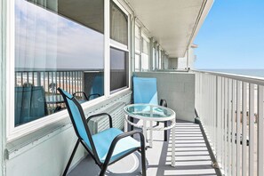 A balcony with a glass table and chairs, overlooking a beach. - 🏁Daytona Beach Club 614 | Oceanfront Complex + Pool 🌴 (Daytona Beach)