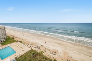 Ein Strandhotel mit Schwimmbad, Liegestühlen und Sonnenschirmen.