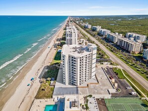Eine Luftaufnahme eines Küstenhotels mit Strandlage, inklusive eines großen Pools, mehrerer Parkplätze und einem markanten Wolkenkratzer.