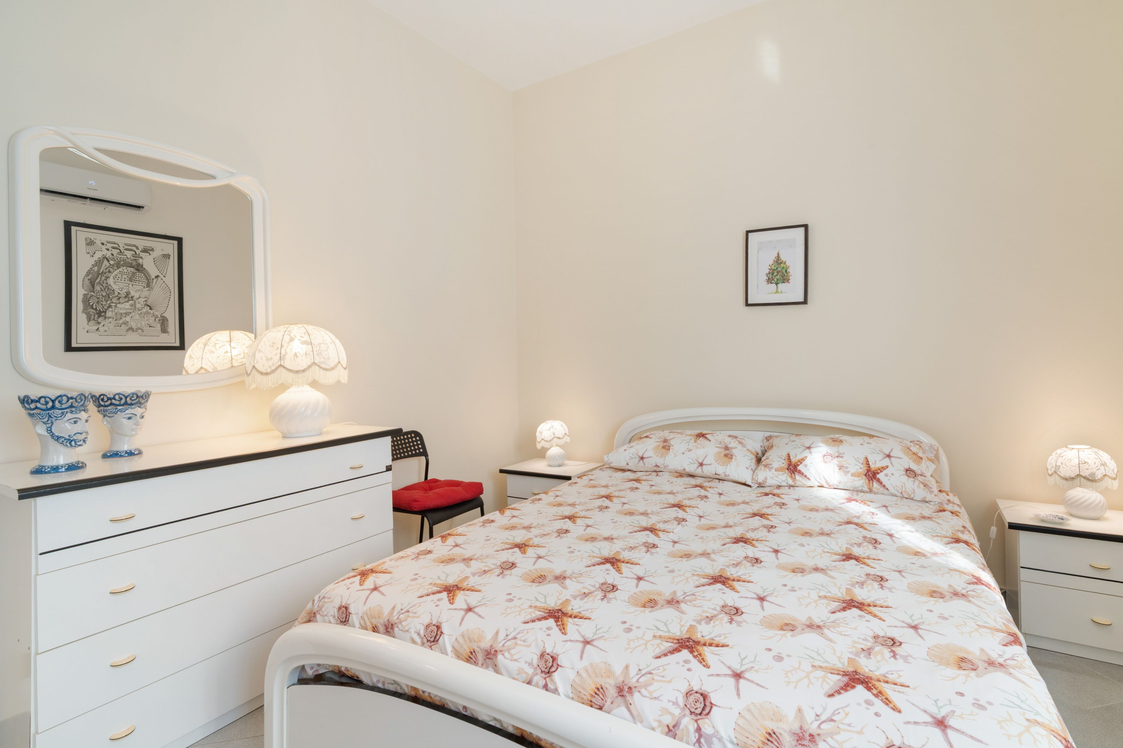 A bedroom with a bed, a dresser, a chair, a nightstand, a lamp, and a framed picture on the wall.