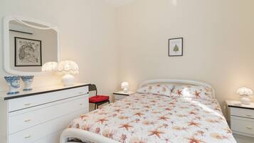 A bedroom with a bed, a dresser, a chair, a nightstand, a lamp, and a framed picture on the wall.