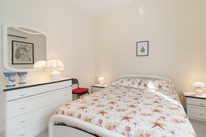 A bedroom with a bed, a dresser, a chair, a nightstand, a lamp, and a framed picture on the wall.