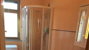 Een badkamer met douchecabine, twee toiletten, een wastafel en een raam.