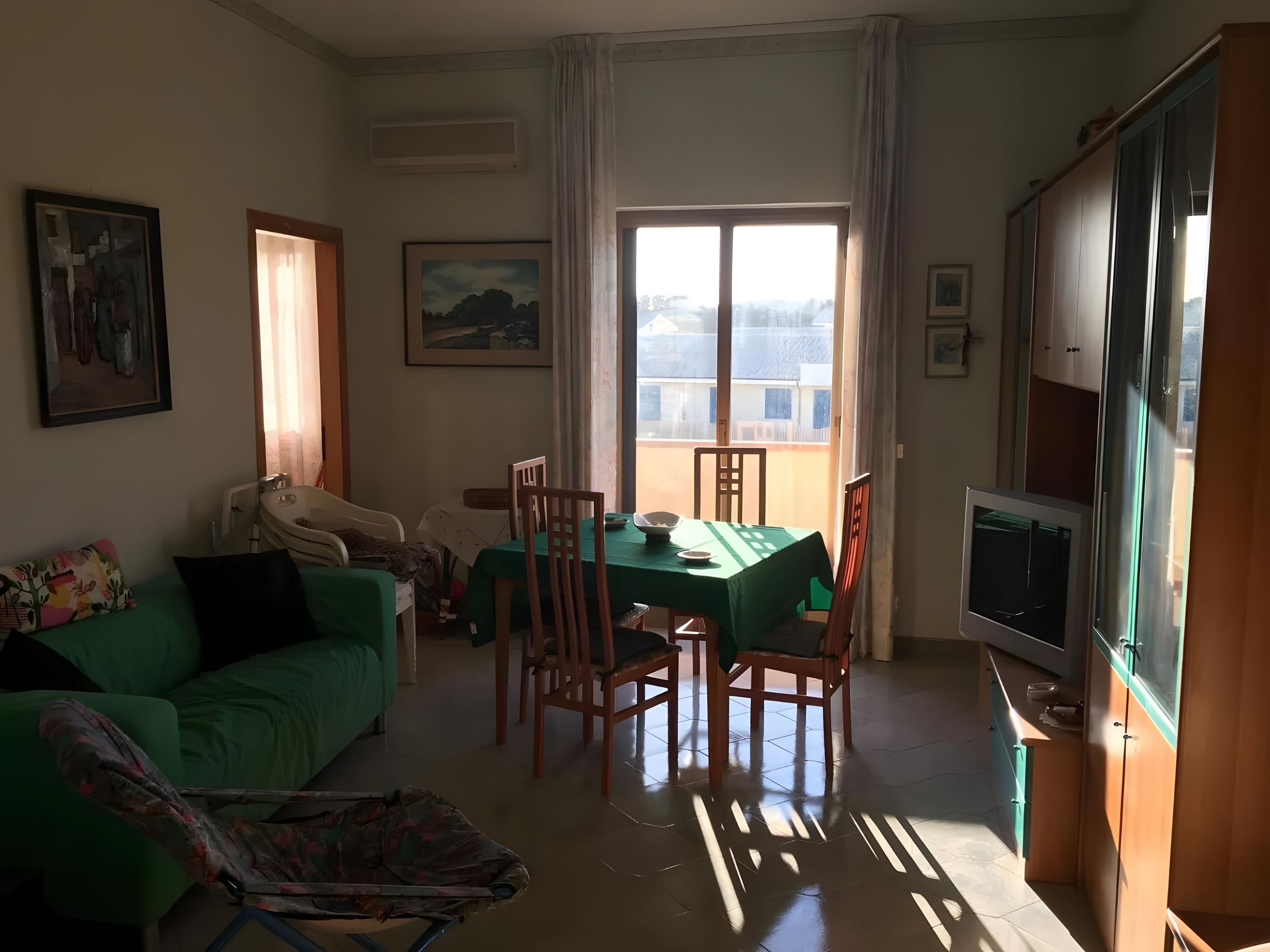 Een woonkamer met een groene bank, een eettafel met stoelen, een kinderwagen en een televisie op een houten kast.