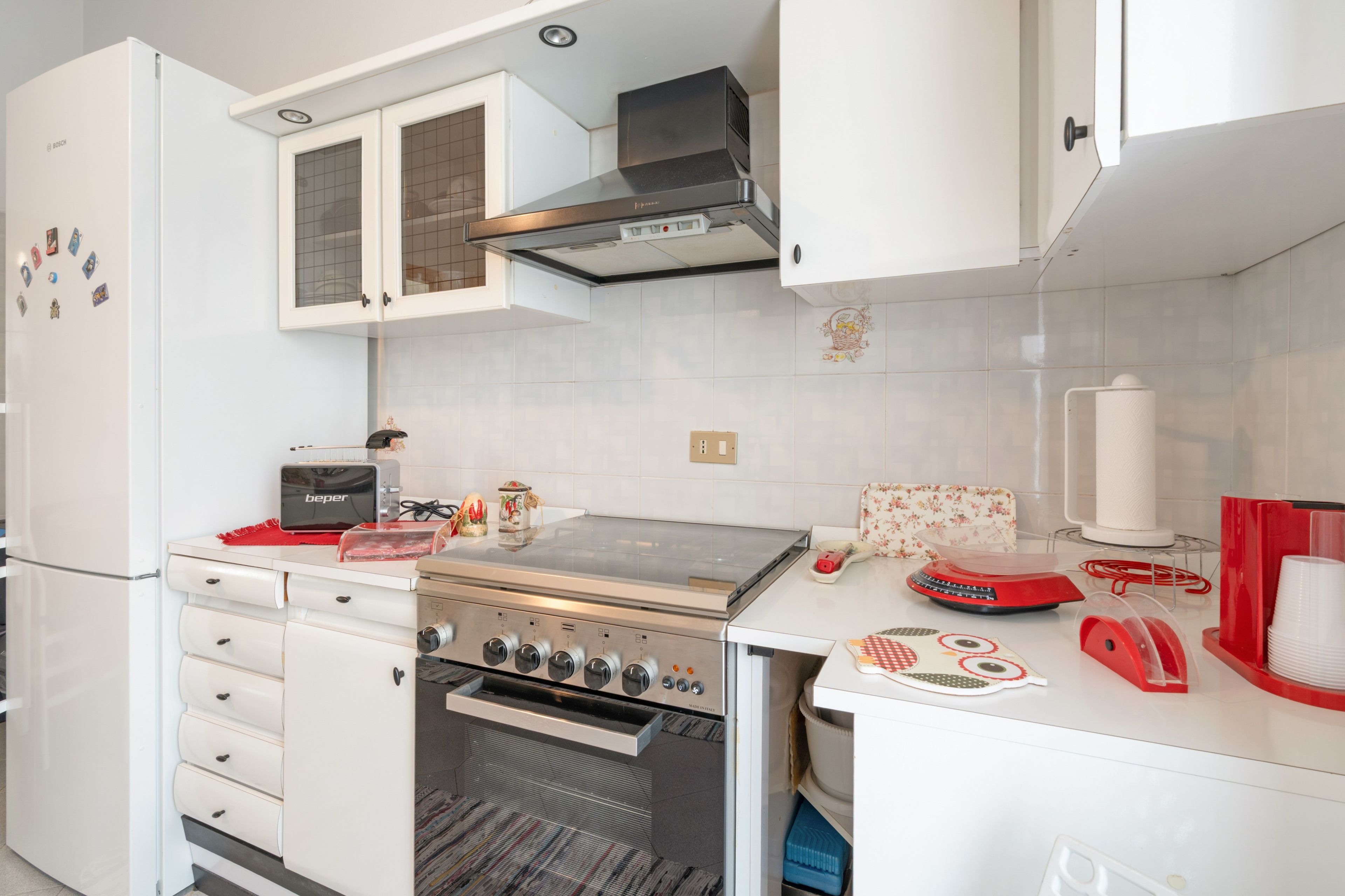 Eine Küche mit weißen Schränken, einem Bosch-Kühlschrank, einem Toaster, einem Herd und einer roten Kaffeemaschine.