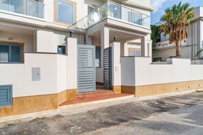 A modern two-story building with a gated entrance, a balcony, and a palm tree.