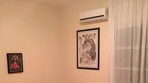Een slaapkamer met een bed, een nachtkastje, een airconditioning en twee ingelijste foto's aan de muur.