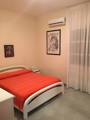 A bedroom with a bed, a nightstand, an air conditioning unit, and two framed pictures on the wall. - MareMilia Home Apartment with Balcony and Air Conditioning (Calabernardo)