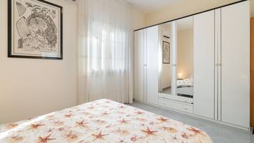 A bedroom with a bed, a wardrobe, a mirror, and a framed picture on the wall.