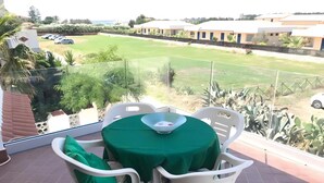 Een balkon met een tafel en stoelen, uitzicht op een groen gazon en een gebouw op de achtergrond.