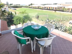 A balcony with a table and chairs, a view of a green lawn, and a building in the background. - MareMilia Home Apartment with Balcony and Air Conditioning (Calabernardo)