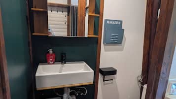 Une petite salle de bain avec un lavabo blanc, un miroir encadré en bois, des toilettes et une petite étagère portant l’inscription « MAGAZINES ».