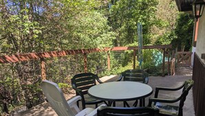 Een terras buiten met een ronde tafel en stoelen, omgeven door een houten omheining en groen.
