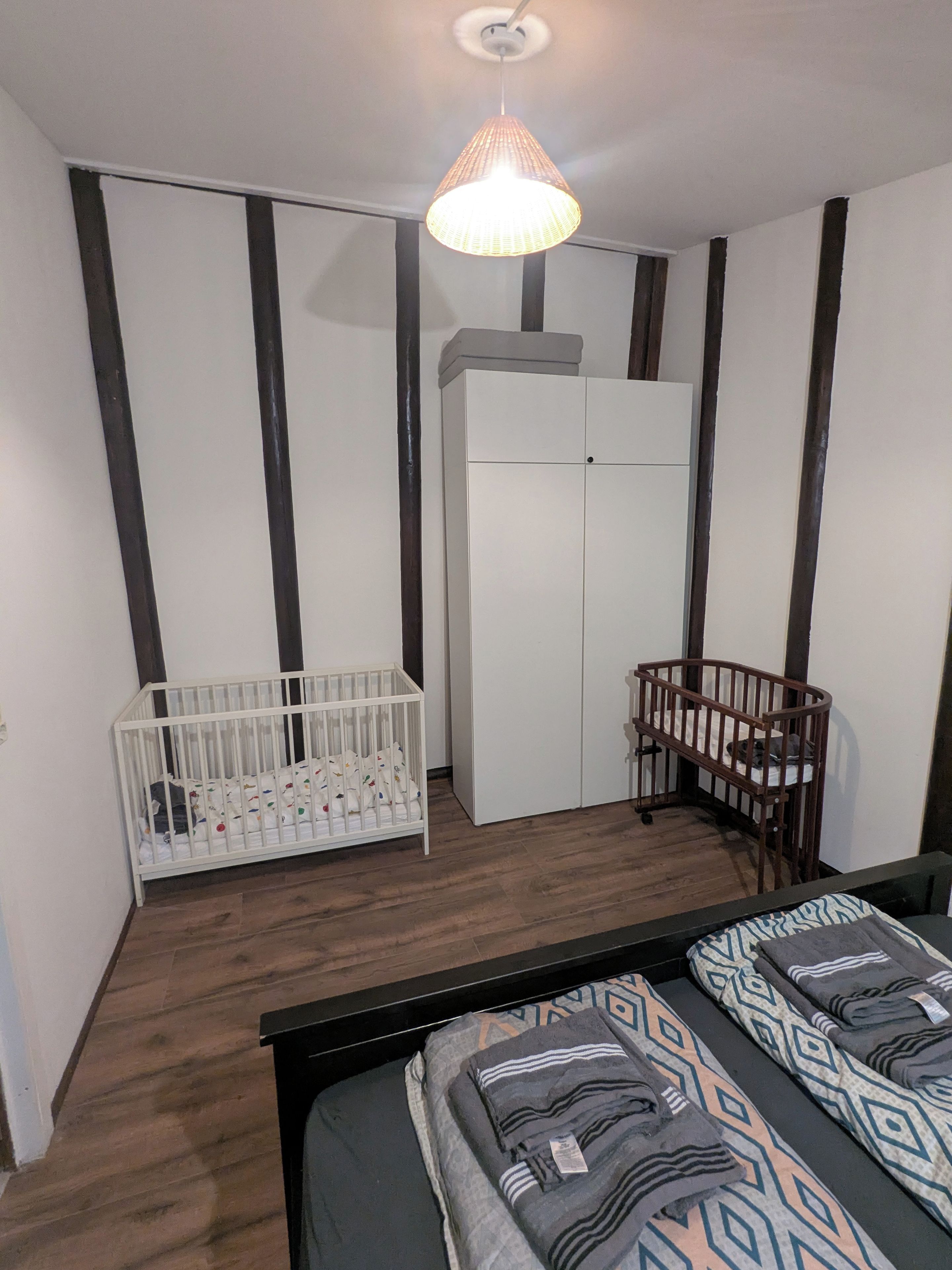 Ein Zimmer mit einem Reisebett, einem Kleiderschrank und einem Bett mit gemusterten Bettbezügen.