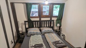 Een tweepersoonsbed met beddengoed met een patroon, een nachtkastje met een lamp en een raam met gordijnen.