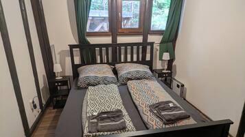 En dobbeltseng med mønstret sengetøj, et sengebord med lampe og et vindue med gardiner.