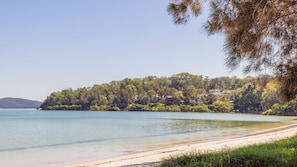A beach with clear water, a sandy shore, and a forested hill with buildings. - HighTide, 142 Sandy Point Rd - romantic getaway on the waterfront (Corlette)