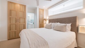 Un dormitorio con una cama grande, un armario de madera y un baño visible a través de una puerta abierta.