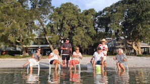 A group of people sitting on chairs in shallow water with trees and buildings in the background. - HighTide, 142 Sandy Point Rd - romantic getaway on the waterfront (Corlette)