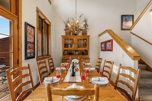 Ein Esszimmer mit einem Holztisch, gedeckt für sechs Personen, flankiert von Holzstühlen, einer Chandelieber und einem Holzkabinett mit Glastüren.