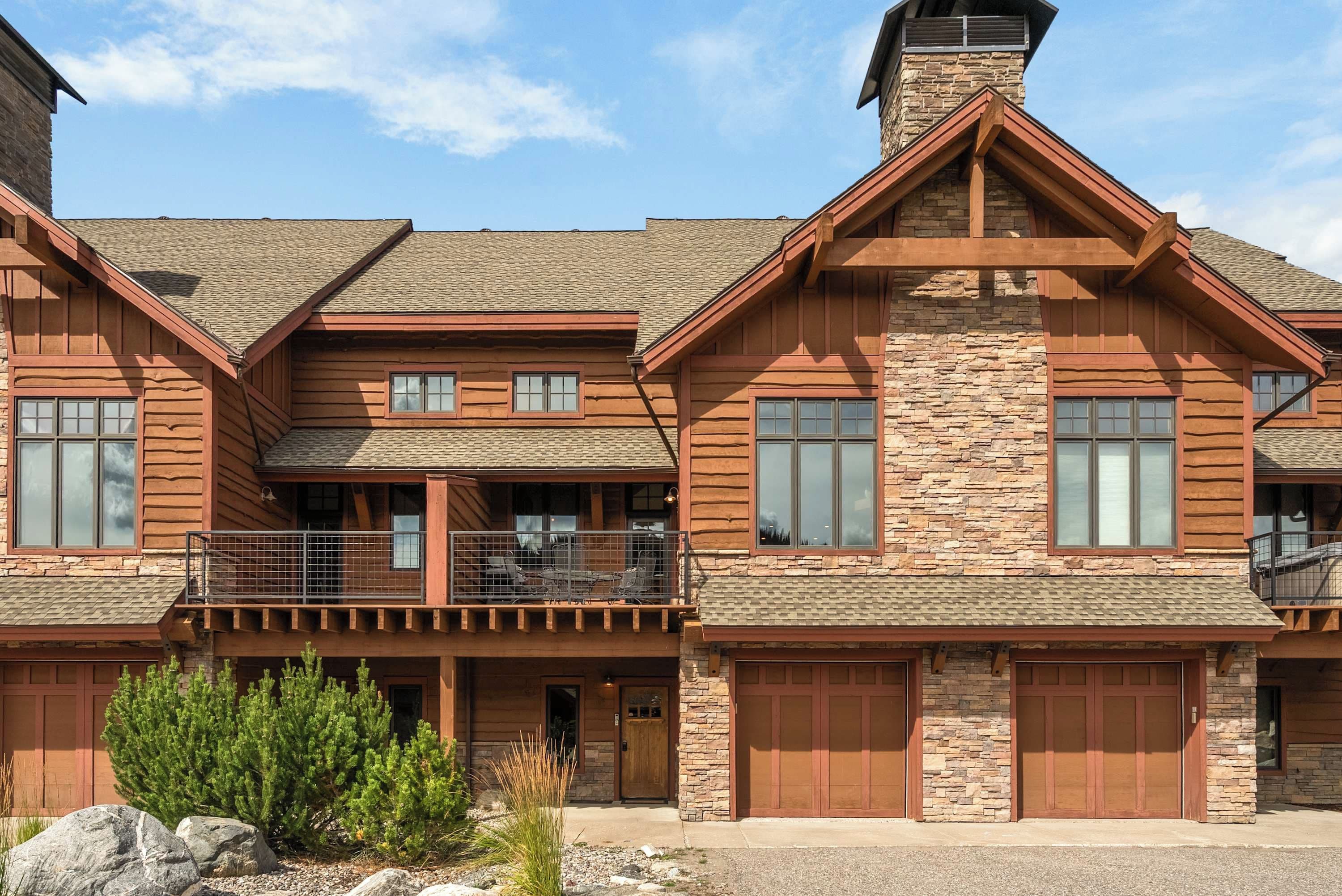 A two-story log cabin with a stone facade, large windows, and a covered patio area.