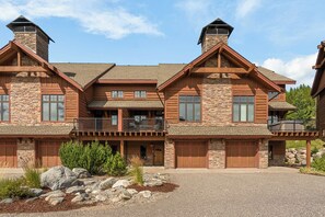 Een groot, meerhoog chalet met stenen accenten, meerdere garage deuren en een overdekte veranda.
