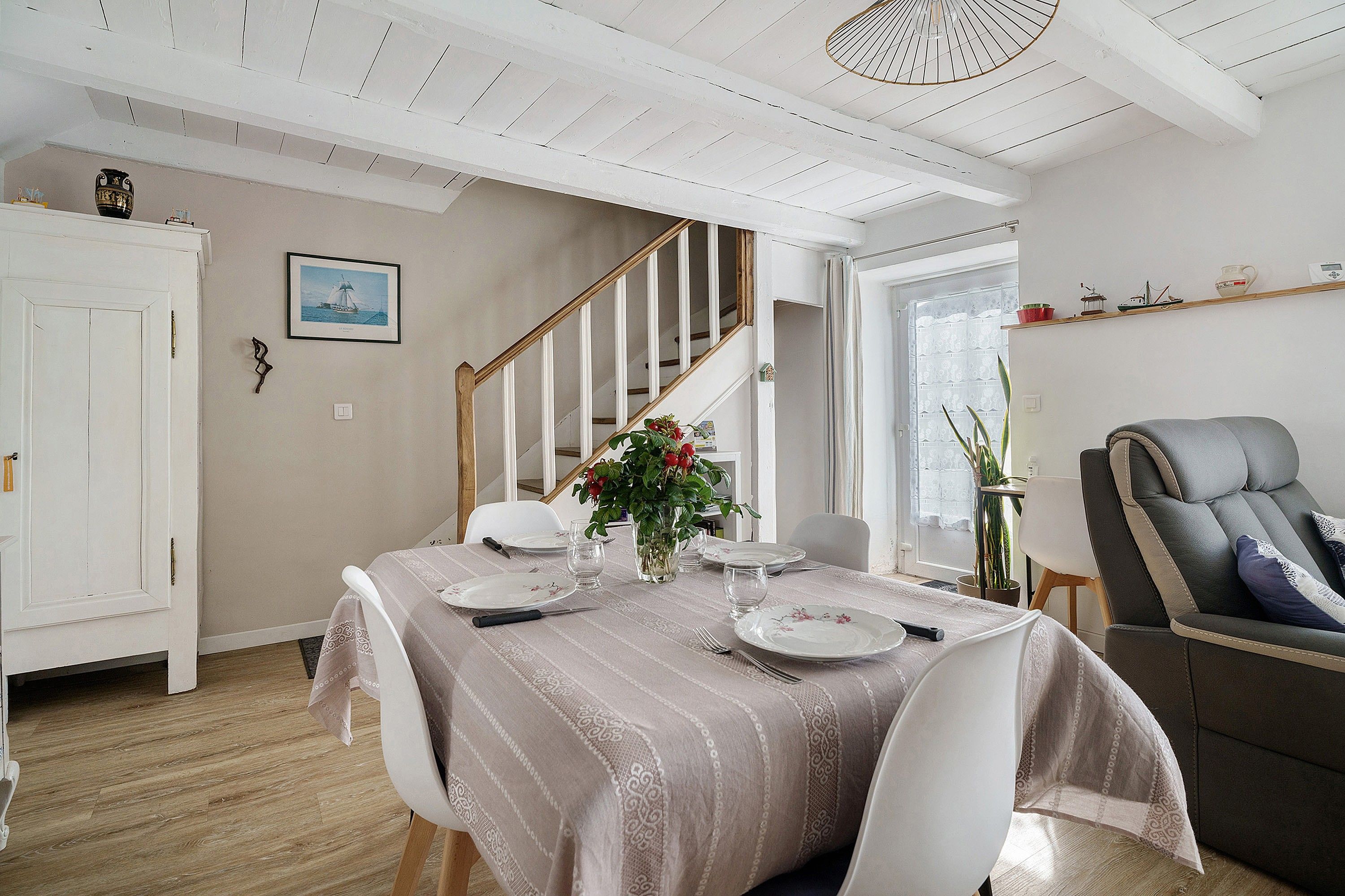 A dining area with a table set for four, a staircase, and a seating area with a chair.