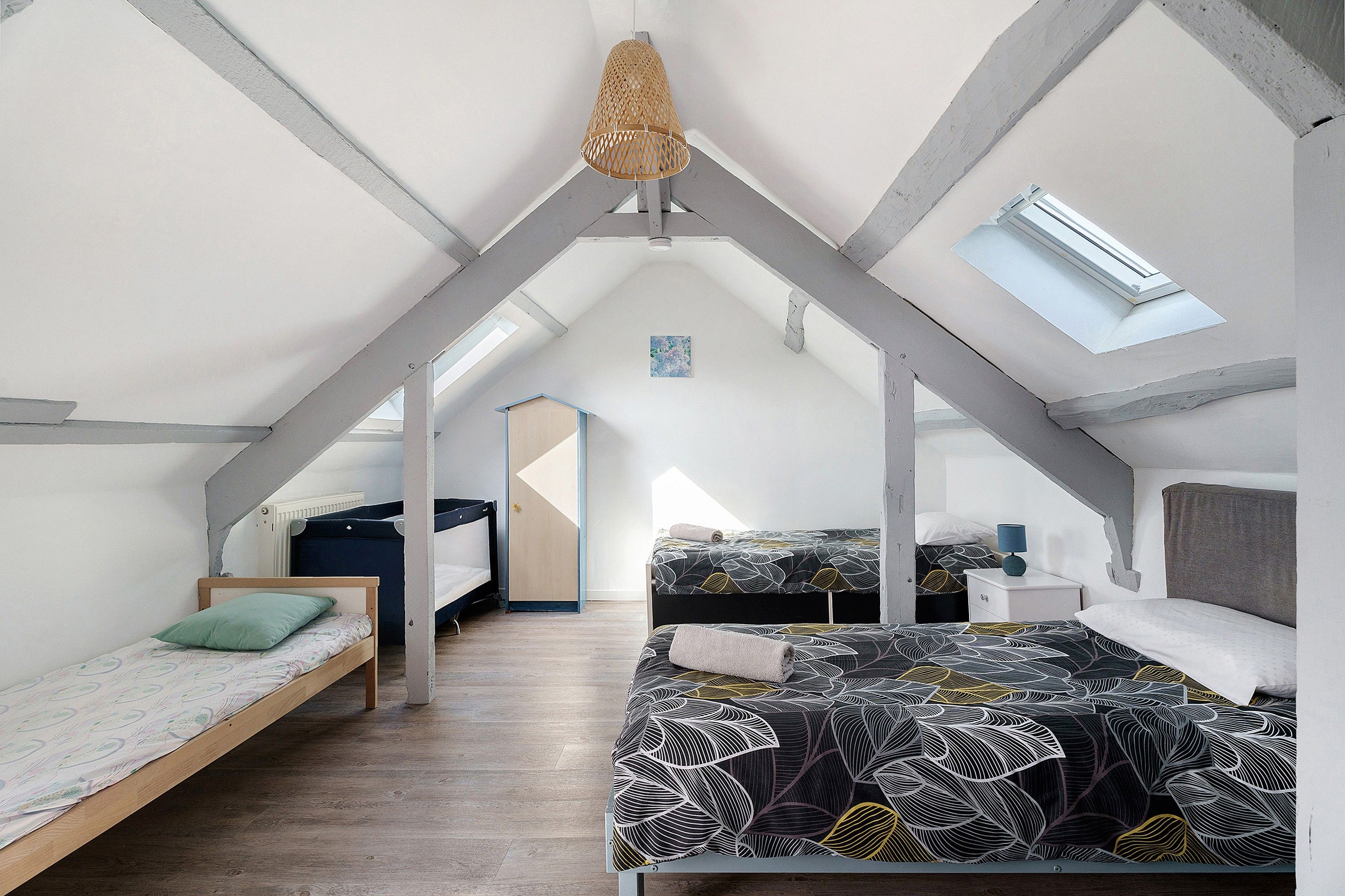 A loft bedroom with a sloped ceiling, a skylight, and a bed with a leaf-patterned bedspread.