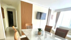 Uma sala de jantar moderna com mesa de mármore, cadeiras de madeira e televisão de tela plana na parede.