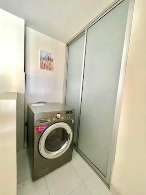 Un lavadero pequeño con lavadora de carga frontal, pared con azulejos y puerta corredera.