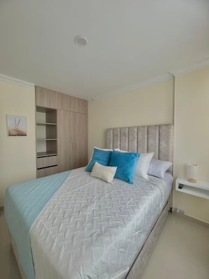Quarto com cama, cabeceira, guarda-roupa e mesa de cabeceira.