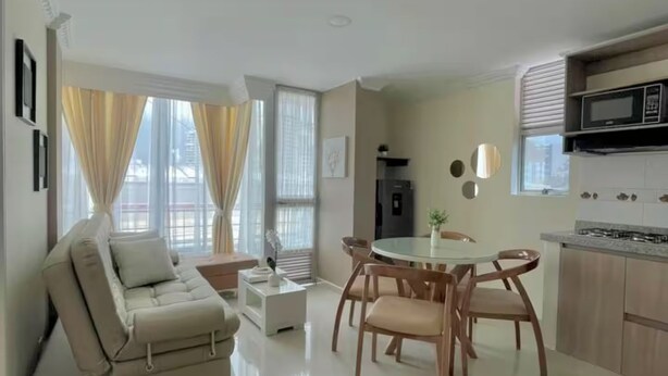Un salon moderne comprenant un canapé, une table à manger et des chaises, une cuisine avec une cuisinière et de grandes fenêtres avec des rideaux.