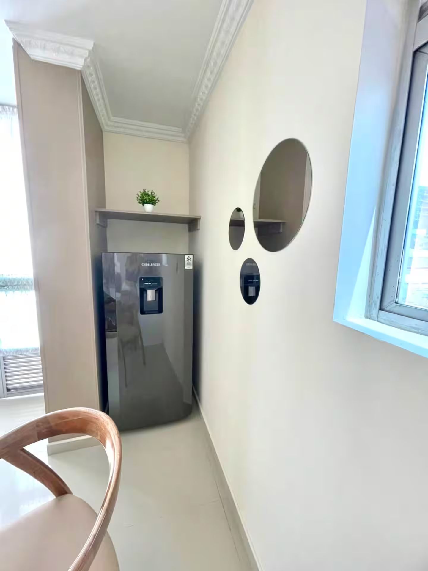 Una cocina compacta con refrigerador integrado, una pequeña planta en maceta sobre la encimera y una ventana que proporciona luz natural.