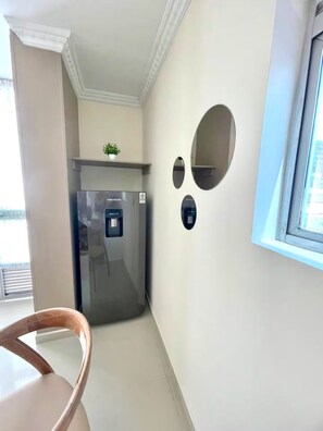 Cozinha compacta com geladeira embutida, um pequeno vaso com planta no balcão e janela que oferece luz natural.