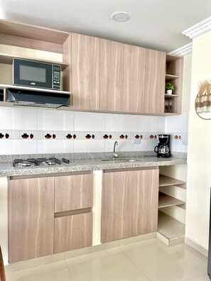 Cozinha com armários de madeira, micro-ondas, cafeteira e painel de azulejos.