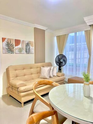 Una sala de estar con un sofá color beige, una mesa redonda de vidrio y un ventilador.