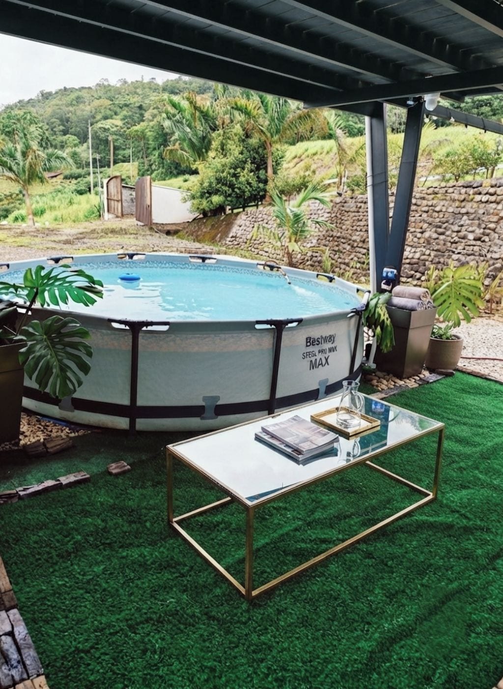 Ein Pool im Freien mit Glastisch und -stühlen, umgeben von Grünpflanzen und einer Steinmauer.