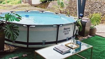 Ein Pool im Freien mit Glastisch und -stühlen, umgeben von Grünpflanzen und einer Steinmauer.