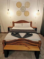 Una cama con estructura de madera, colchón blanco y manta gris. Hay dos mesitas de noche con lámparas.