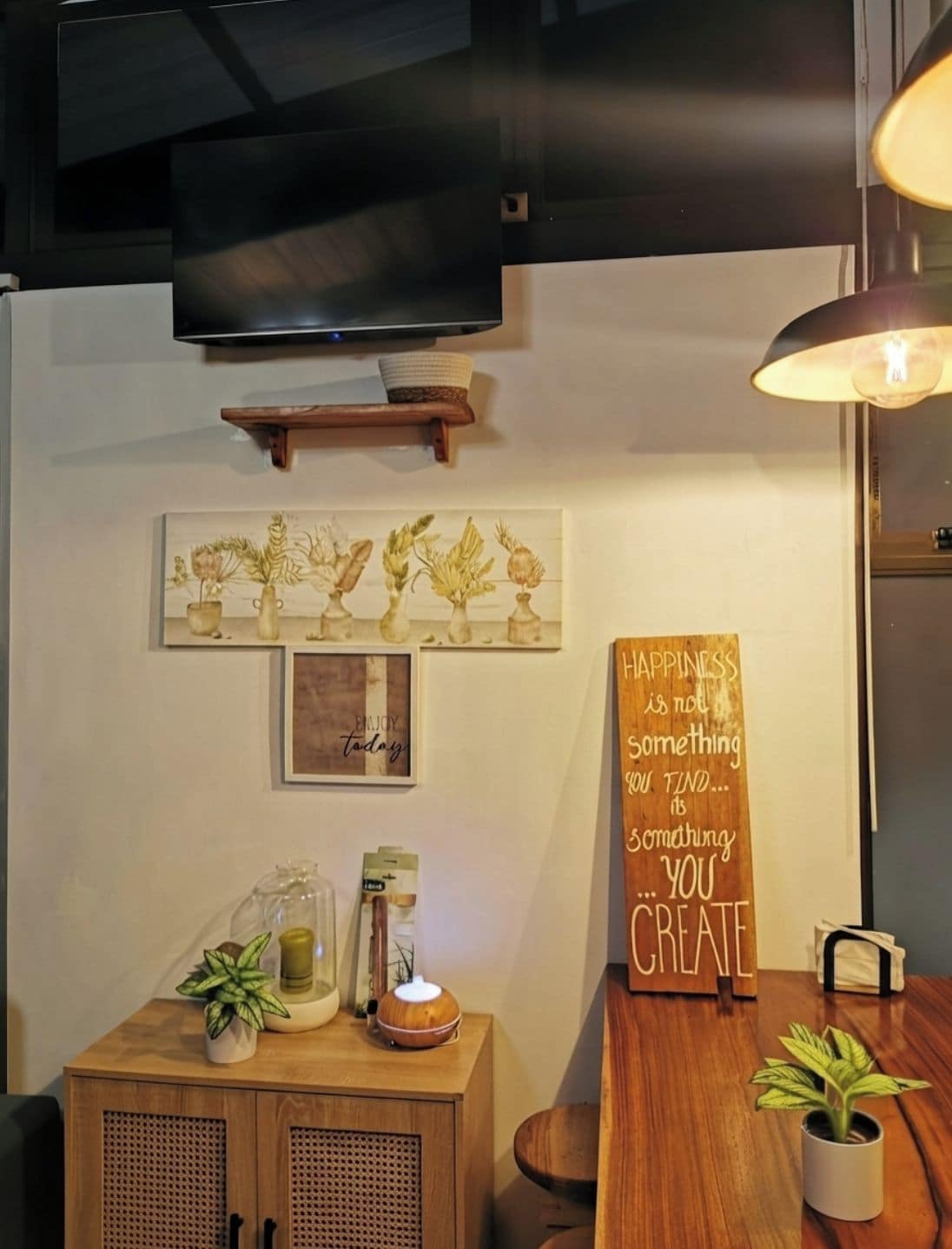 Une pièce chaleureuse avec un meuble en bois, un téléviseur fixé au mur et un panneau affichant une citation inspirante.