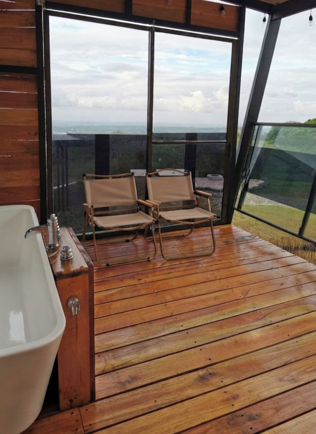 Un terrazza in legno con una grande finestra, una vasca da bagno e due sedie rivolte verso il panorama.