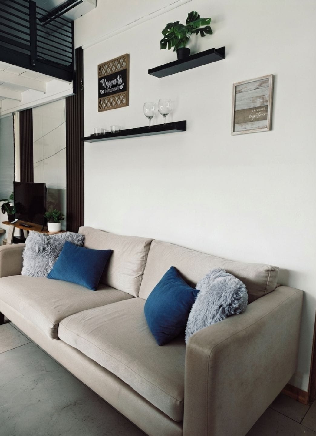 Un divano beige con cuscini blu e grigi, una piccola pianta e due elementi decorativi appesi alla parete.