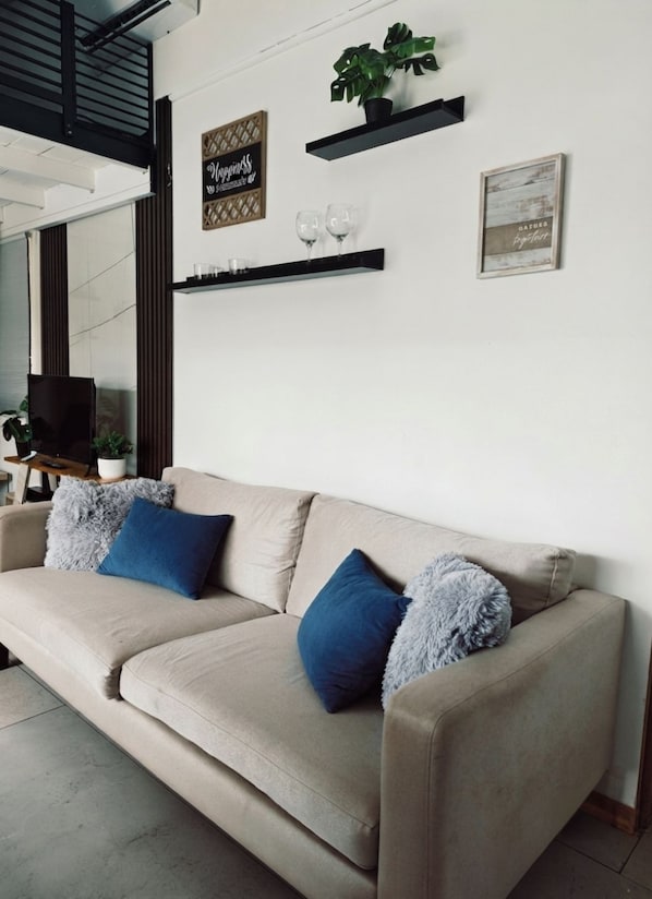 A beige sofa with blue and grey pillows, a small plant, and two framed items on the wall.