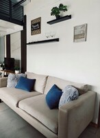 A beige sofa with blue and grey pillows, a small plant, and two framed items on the wall.