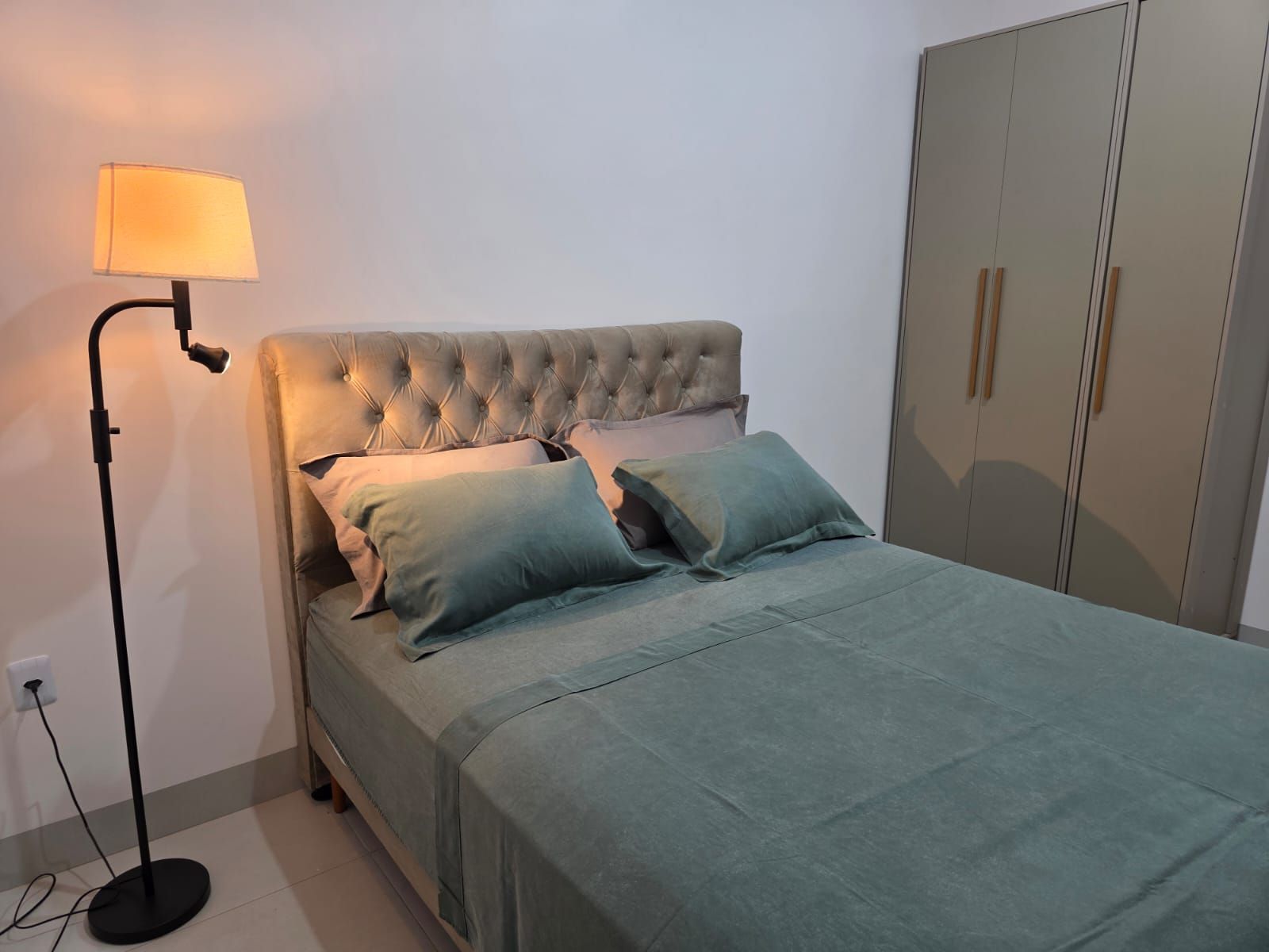 A bed with a tufted headboard, two pillows, a floor lamp, and a wardrobe.