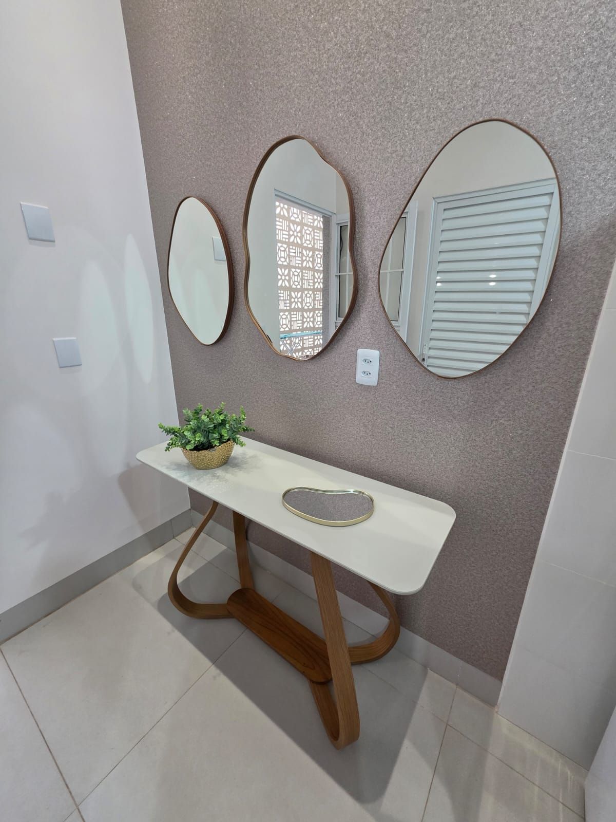 A hallway with a white console table, a potted plant, and three wall-mounted mirrors.