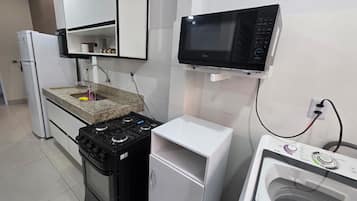 Cozinha compacta com fogão a gás, micro-ondas e máquina de lavar embutida.